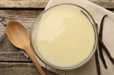 Yoğun süt, kaşık ve vanilya kapsülleri ahşap masada, düz yerde.