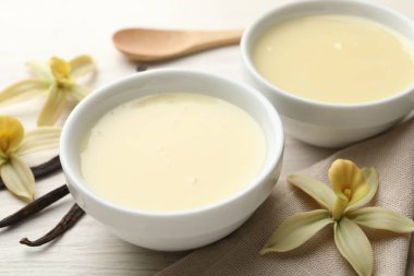 Lezzetli konsantre süt, vanilya kabukları, çiçekler ve kaşık beyaz ahşap masa, yakın plan