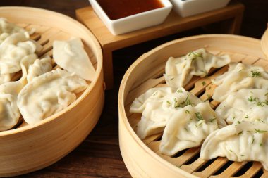 Bambu tencerelerinde kaynamış gyoza (hamur tatlısı) ve ahşap masada sos, yakın plan.