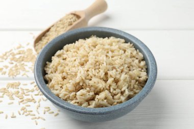 Lezzetli kahverengi pirinç kasede ve çiğ taneler beyaz ahşap masada, yakın plan.