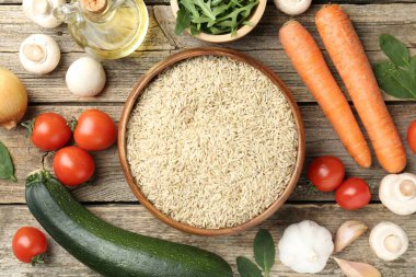 Tabaktaki çiğ kahverengi pirinç taze ürünlerin arasında, ahşap masada, düz yerde.