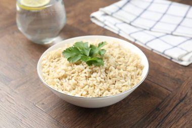 Ahşap masada servis edilen maydanozlu lezzetli kahverengi pirinç, yakın plan.