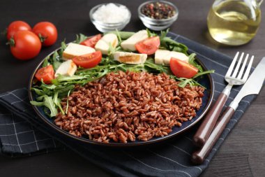 Lezzetli kahverengi pirinç, tavuk, roka ve domatesler siyah ahşap masada, yakın plan.