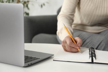 İnternette bilgisayar kullanarak öğrenen ve içerideki beyaz masada notlar alan bir kadın. Kendi kendine çalışma.