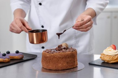 Pasta şefi pastayı eritilmiş çikolatayla süslüyor. Mutfakta, yakın plan.