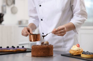 Pasta şefi pastayı eritilmiş çikolatayla süslüyor. Mutfakta, yakın plan.