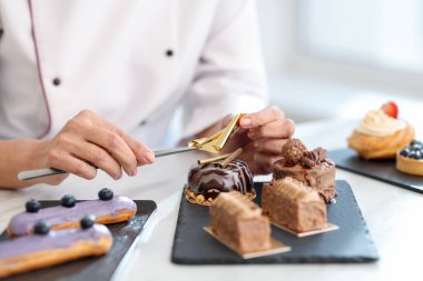 Pasta şefi mutfaktaki masada yenilebilir altın yaprak örtüsüyle lezzetli tatlılar hazırlıyor.