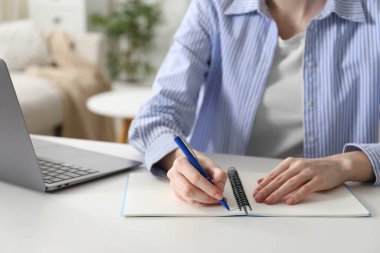 Beyaz masa içerisindeki çevrimiçi derste not alan bir kadın, yakın plan. Kendi kendine çalışma.