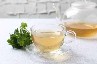 Cam bardakta Aromatik bitki çayı, taze maydanoz ve açık gri masada çaydanlık, yakın plan.
