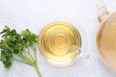 Cam bardakta Aromatik bitki çayı, taze maydanoz ve açık gri masada çaydanlık, düz uzanmış