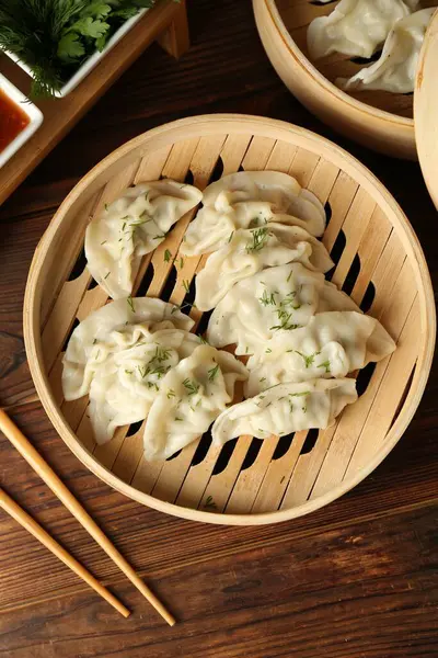 Bambu buharlı buharda kaynamış gyoza (hamur tatlısı), sos ve çubuklar ahşap masada, düz yerde.