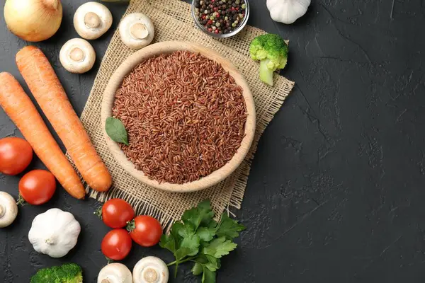 Tabaktaki çiğ kahverengi pirinç taze ürünlerin arasında koyu dokulu masada, düz yerde. Metin için boşluk