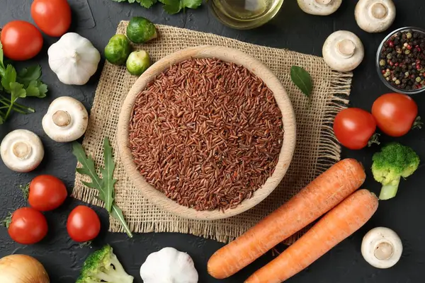 Tabaktaki çiğ kahverengi pirinç taze ürünlerin arasında koyu dokulu masada, düz yerde.