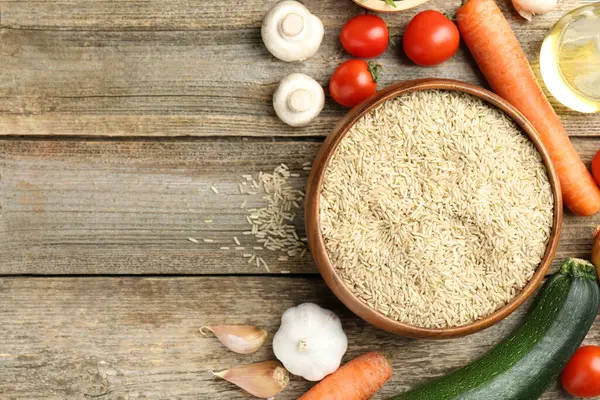 Tabaktaki çiğ kahverengi pirinç ahşap masadaki taze ürünlerin arasında, düz yerde. Metin için boşluk