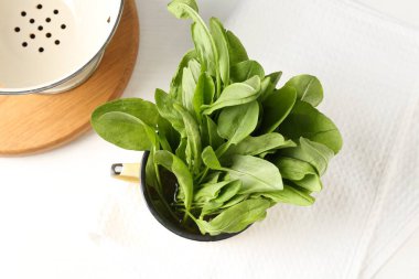 Taze kuş yaprakları kasede ve kevgir beyaz masada, düz yatıyordu.