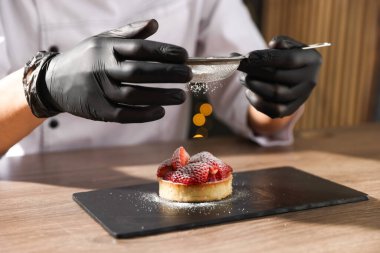 İçerideki ahşap masadaki turtaya şeker serpiştiren şekerci, yakın plan.