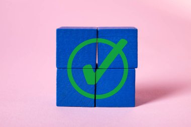 Onaylandı. Pembe arka planda tahta küplerden yapılmış yeşil kontrol işareti