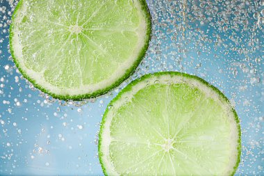 Açık mavi arka planda limon dilimli soda, yakın plan.