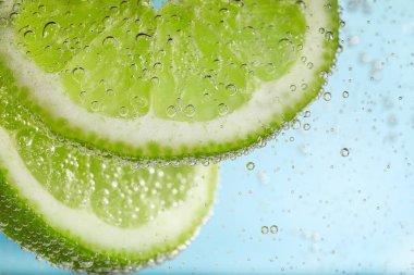 Açık mavi arka planda limon dilimli soda, yakın plan.
