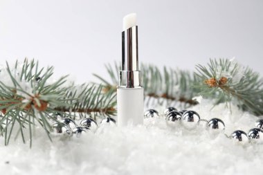 Nemlendirici dudak kremi, Noel dekorasyonu ve beyaz arka planda suni kar üzerindeki köknar ağacı dalları, yakın plan. Kış bakımı