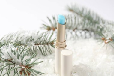 Nemlendirici dudak kremi ve suni kar üzerindeki köknar ağacı dalları beyaz arka planda, yakın plan. Kış bakımı