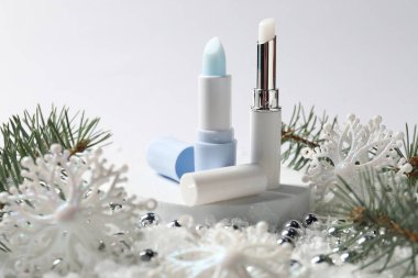Nemlendirici dudak kremleri, Noel dekorasyonu ve beyaz arka planda suni kar üzerindeki köknar ağacı dalları, yakın plan. Kış bakımı