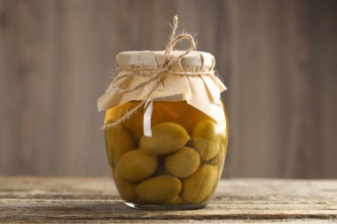 Ahşap masada cam kavanozda turşulu yeşil zeytin, yakın plan.