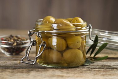 Cam kavanozda turşulu yeşil zeytin ve ahşap masada baharatlar, yakın plan.
