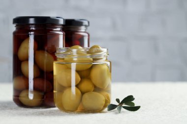 Kavanozlarda yeşil zeytin turşusu ve beyaz desenli masada yapraklar, yakın plan. Metin için boşluk