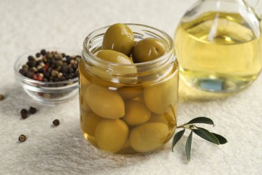 Kavanozda turşulu yeşil zeytin, beyaz desenli masada yağlı ve biberli mısır, yakın plan.