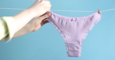 Açık mavi arka planda çamaşır ipine güzel külot asan bir kadın.
