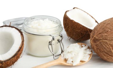 Kavanozda hindistan cevizi pişirme yağı, kaşık ve ahşap masada beyaz arka planda taze meyveler.