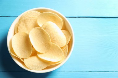 Açık mavi ahşap masada, tabakta patates cipsi, üst manzara. Metin için boşluk