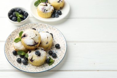 Yaban mersinli lezzetli kekler, pudra şekeri ve beyaz ahşap masada nane şekeri, yakın plan. Metin için boşluk