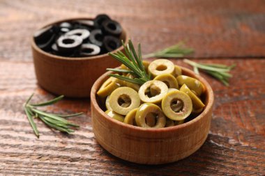 Farklı lezzetlerde marine edilmiş zeytin halkaları ve ahşap masada biberiye, yakın plan.