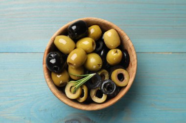 Farklı lezzetlerde marine edilmiş zeytin halkaları ve biberiyeler açık mavi ahşap masada, üst tarafta.