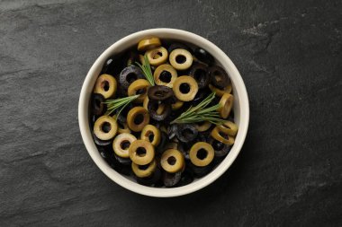 Farklı lezzetli salamura zeytin halkaları ve biberiye kasede koyu dokulu masa, üst manzara.