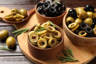 Farklı lezzetlerde marine edilmiş zeytin halkaları, tüm olanlar ve ahşap masada biberiye, yakın plan.