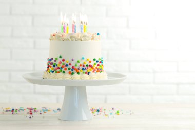 Renkli serpilmiş nefis bento keki ve beyaz tuğla duvara karşı açık ahşap masada yanan mumlar. Metin için boşluk