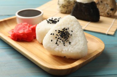 Pirinç topları (onigiri), soya sosu ve açık mavi ahşap masa üzerinde turşulu zencefil, yakın plan. Geleneksel Japon yemeği