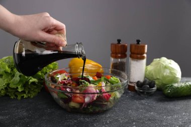 Koyu dokulu masada salataya balzamik sirke döken kadın, yakın plan, gri arka plan...