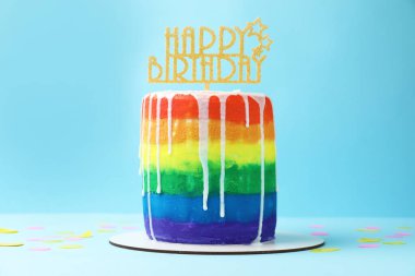 Lezzetli gökkuşağı doğum günü pastası ve açık mavi arka planda konfeti.