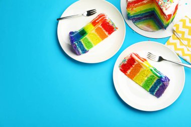 Açık mavi masada servis edilen leziz gökkuşağı pastasından parçalar. Metin için boşluk