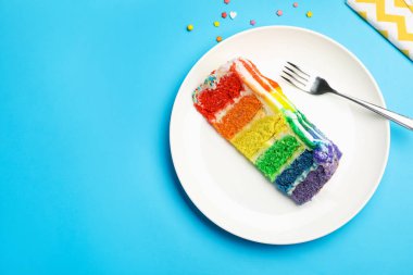 Lezzetli bir parça gökkuşağı pastası ve açık mavi masaya serpiştirilmiş şekerleme. Metin için boşluk