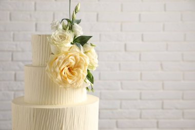 Beyaz tuğla duvarın yanında çiçeklerle süslenmiş nefis düğün pastası, yakın plan. Metin için boşluk