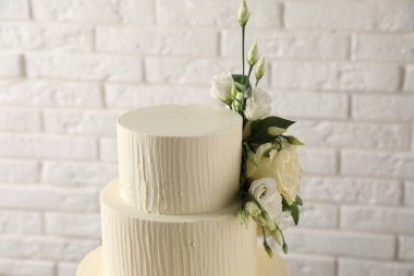 Beyaz tuğla duvarın yanında çiçeklerle süslenmiş nefis düğün pastası, yakın plan.