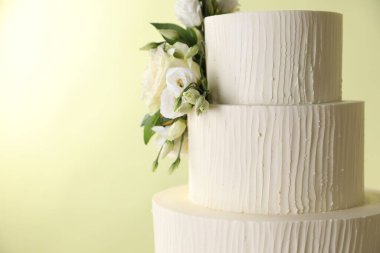 Açık yeşil arka planda çiçeklerle süslenmiş nefis bir düğün pastası. Yakın plan. Metin için boşluk