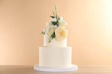 Ahşap masada bej arka planda çiçeklerle süslenmiş nefis düğün pastası, yakın plan.