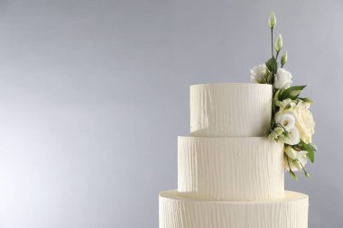 Gri arka planda çiçeklerle süslenmiş lezzetli düğün pastası, yakın plan. Metin için boşluk