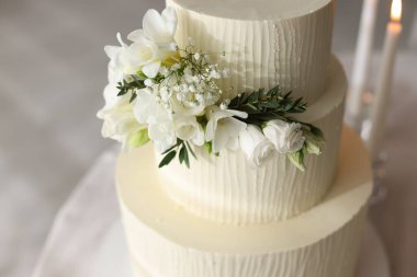 Çiçek desenli nefis düğün pastası ve kapalı bir masada yanan mumlar.